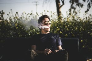 Man exhaling vapor while relaxing outdoors with a THC vape.