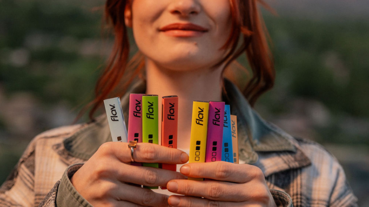 Woman holding a variety of Flav disposable vape pens in different flavors.