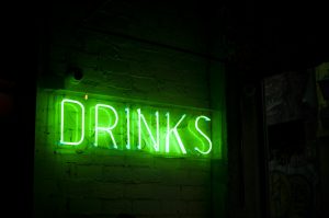 Green neon sign that reads 'DRINKS' in a dimly lit setting.