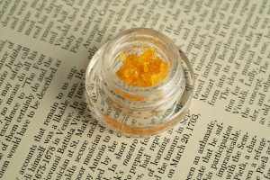 Jar of golden live resin concentrate on an open book page.